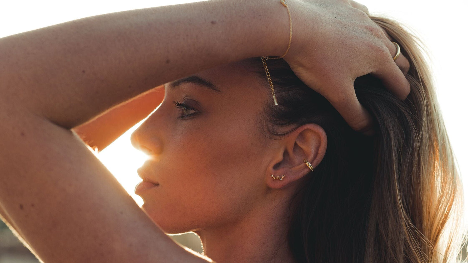Une femme se tient les cheveux pour montrer ses bijoux pendant un coucher de soleil