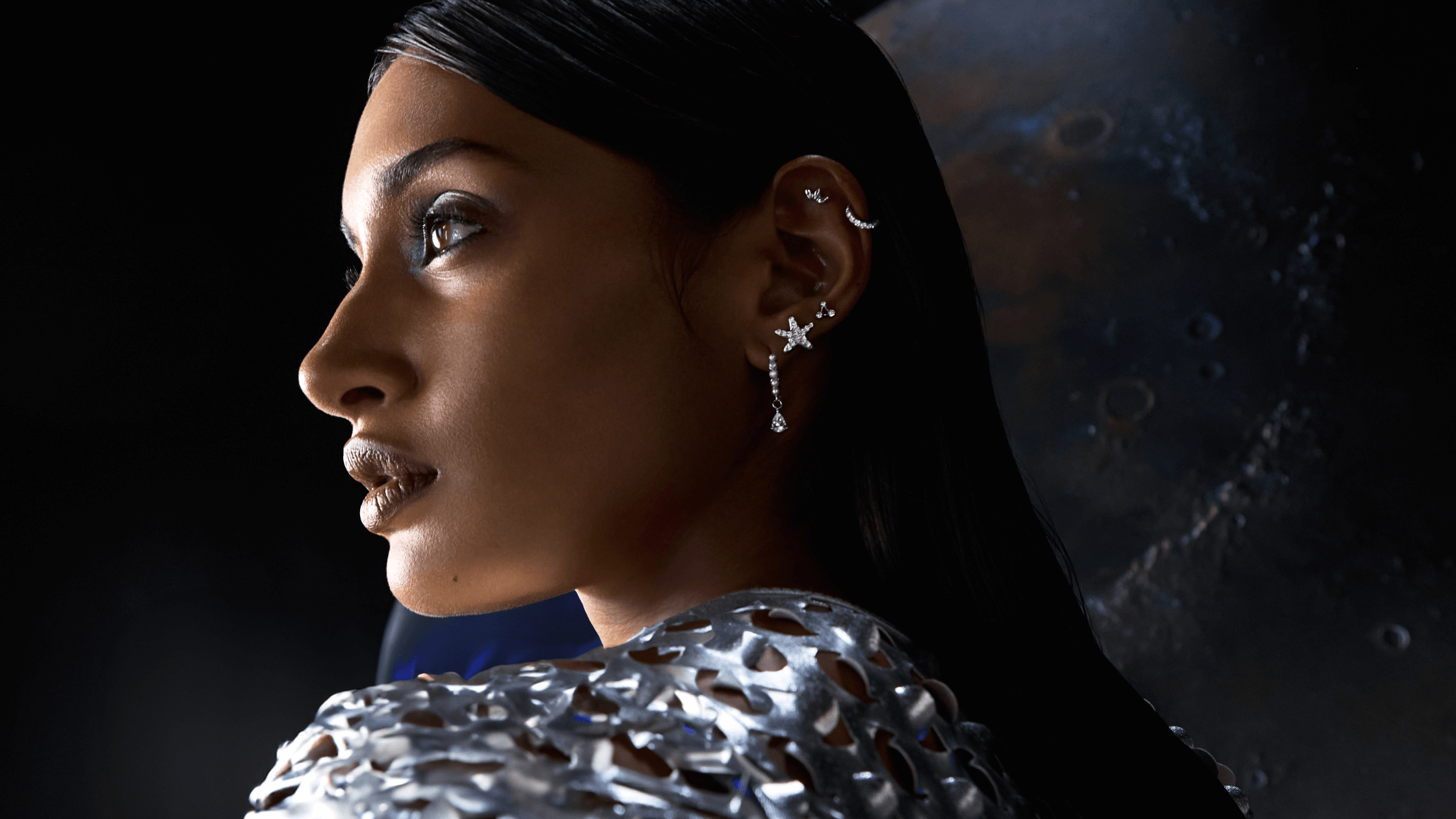 Une femme porte un haut métallique et des bijoux d'oreille en argent