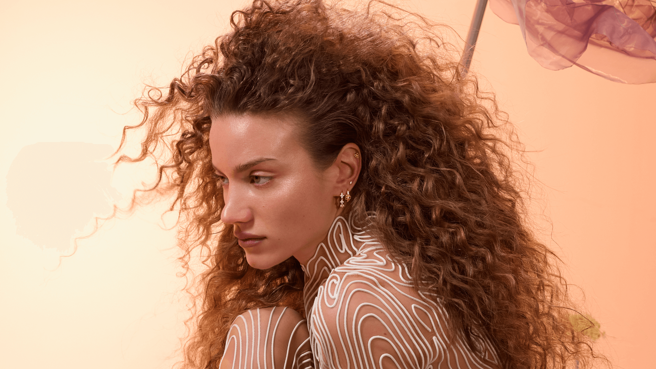 Une femme de profil avec les cheveux ondulés porte des bijoux