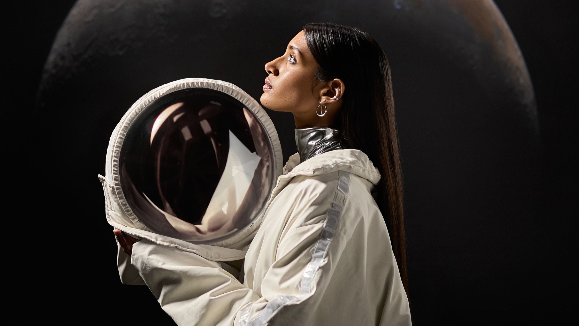 Une femme regarde en l'air elle tient un casque de cosmonaute