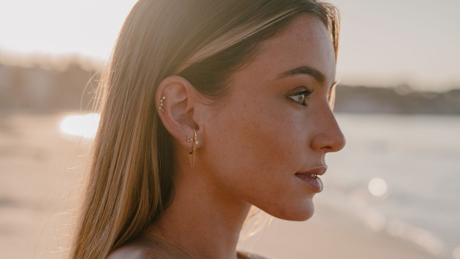 Une femme de profil portant des boucles d'oreilles regarde la mer 