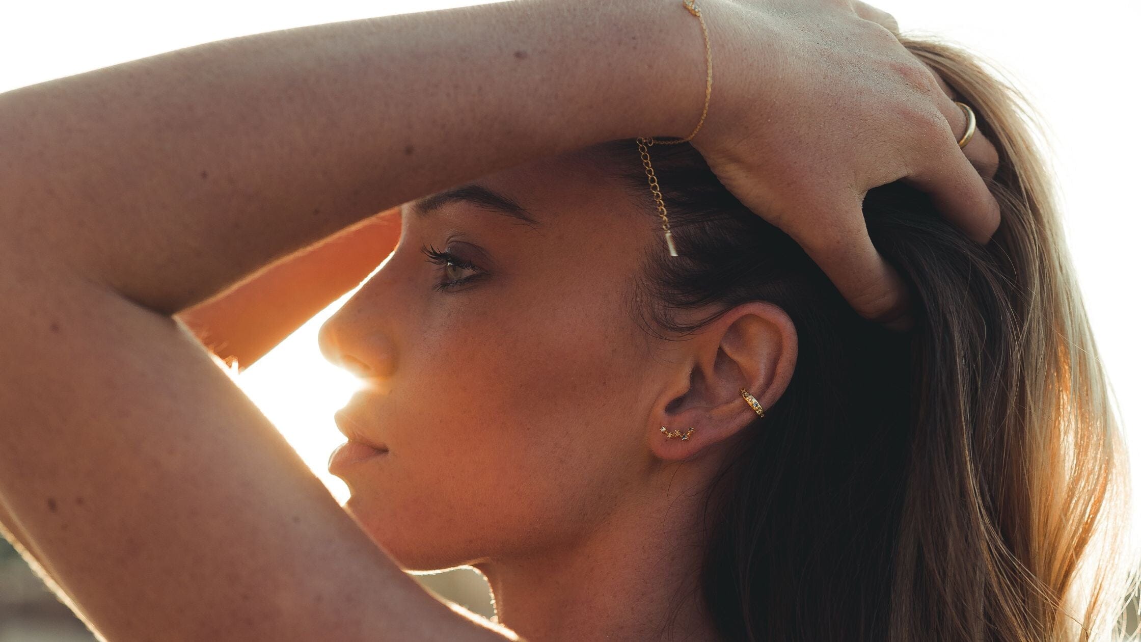 Une femme se tient les cheveux pour montrer ses bijoux pendant un coucher de soleil