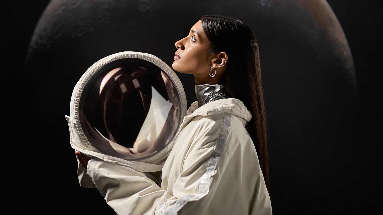 Une femme regarde en l'air elle tient un casque de cosmonaute 